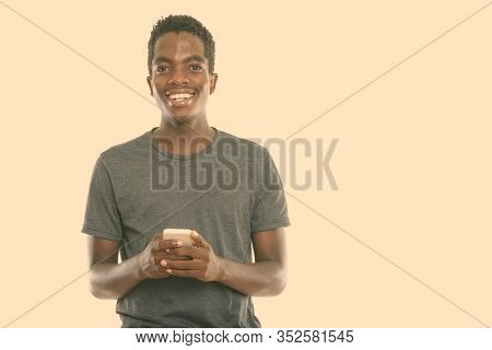 Studio Shot Of Young Hpapy Black African Teenage Boy Smiling While Holding Mobile Phone