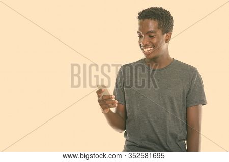 Studio Shot Of Young Hpapy Black African Teenage Boy Smiling While Using Mobile Phone