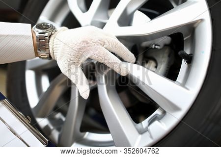 Close-up Of Persons Hand Wearing Work Gloves And Working With Car Wheel. Clipboard With Checklist In