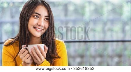 Asian Young Female Holding A Cup Of Coffee In Modern Coffee Shop Or Coworking Space Beside Window Mi