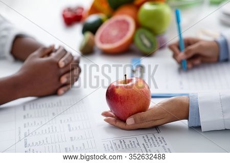Close Up Of Female Afro Doctor Holding Big Fresh Red Apple, Black Lady Having Session With Dietologi