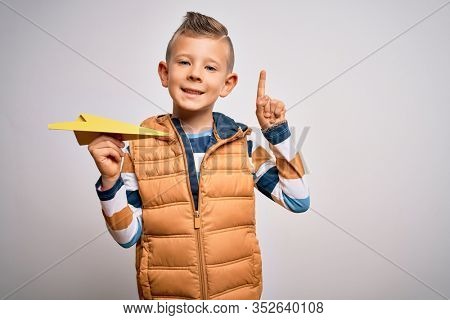 Young little caucasian kid having fun and playing imagination fly with paper plane surprised with an idea or question pointing finger with happy face, number one