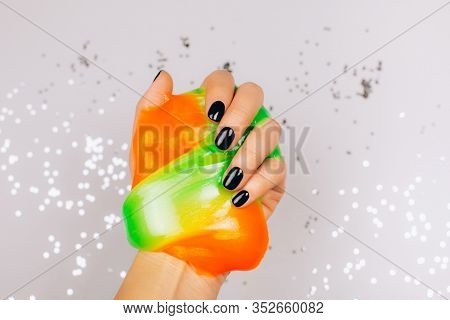 Hands With Black Manicure Holding Slime In Orange And Green Vibrant Colors
