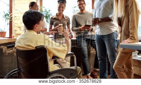 Portrait Of Young Male Office Worker In A Wheelchair Drinking Coffee And Chatting With Colleagues Du