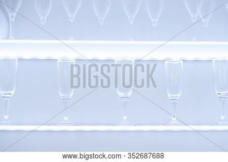 Clean Wine Glasses And Champagne Flutes Upended On A White Wooden Shelf In A Kitchen Or Bar