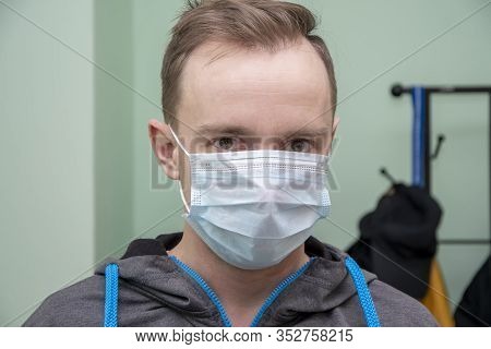 A Young Guy In A Motorcycle With A Hood In A Medical Mask On The Background Of A Concrete Wall. Pers