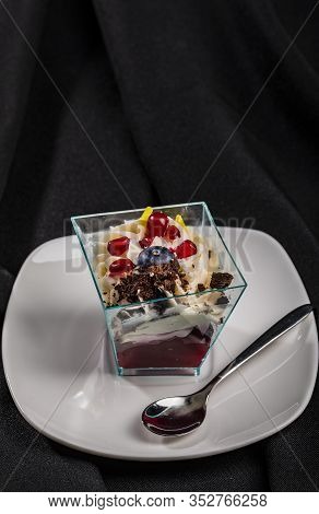 Individual Portion Of Layered Dessert In Trapezoid Glass, White Squared Plate, Isolated Black Fabric