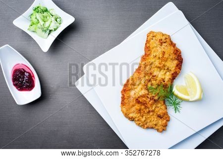 Traditional deep fried Wiener schnitzel from veal topside with cucumber salad and cranberry jam offered as top view on a modern design plate on a rustic wooden board 