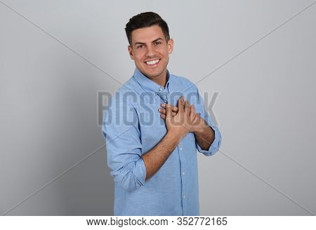 Handsome Grateful Man With Hands On Chest Against Light Grey Background
