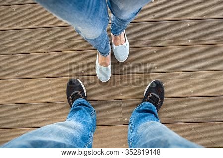 Top Down View Of Legs In Denim Jeans Pants And Light Summer Sneakers Standing On Wooden Floow.