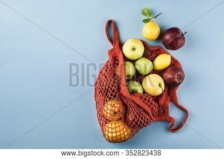 Apples And Lemons In An Orange String Bag On A Blue Background. Top View. Concept Of Life Without Pl