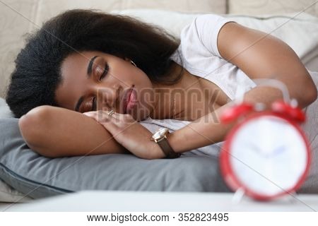 Young Woman Is Sleeping An Alarm Clock Is On Table. Beautiful Girl Takes Every Opportunity To Recove