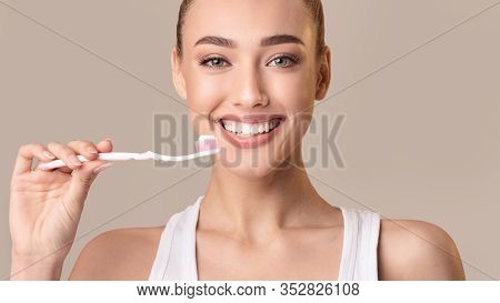 Toothcare. Smiling Girl Holding Toothbrush With Toothpaste Cleaning Teeth Over Beige Studio Backgrou