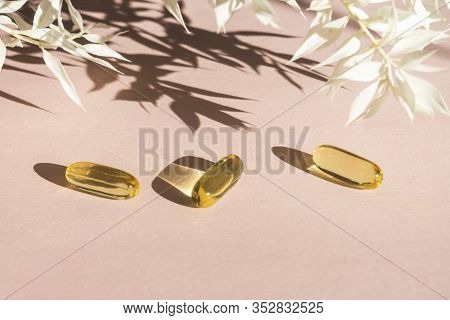 Oil Yellow Gelatin Capsules On Pink Background With Flower Shadow, Vitamins And Antioxidant Concept 