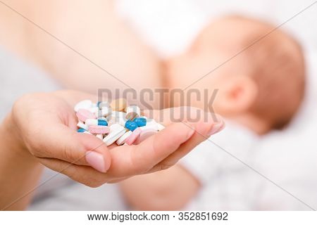 Mother holding handful of pills and tablets while breastfeeding newborn baby. Breastfeeding and medication concept
