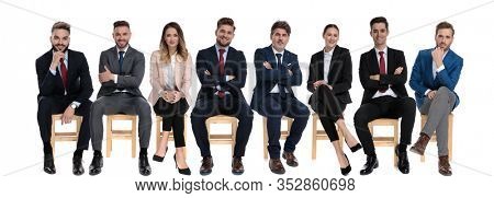 Team of 8 confident businessmen holding their arms crossed and smiling while sitting on chairs on white studio background