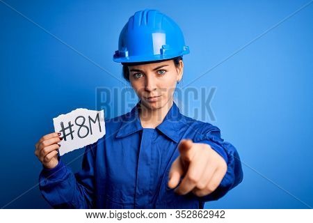 Beautiful worker woman wearing hardhat and uniform celebrating 8th march womens day pointing with finger to the camera and to you, hand sign, positive and confident gesture from the front