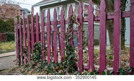 An Oid Worn Red Wooden Fence With A House And A Tree In The Background