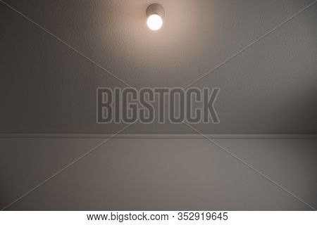Wall and ceiling with bare light bulb lighting on the ceiling. Simple white room.
