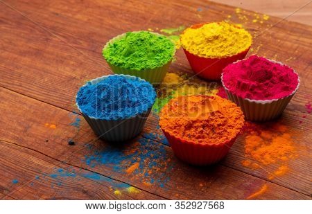 Holi color powder. Organic Gulal colours in bowl for Holi festival, Hindu tradition festive. Blue, pink, magenta, orange, yellow holi dry paints on wood desk background