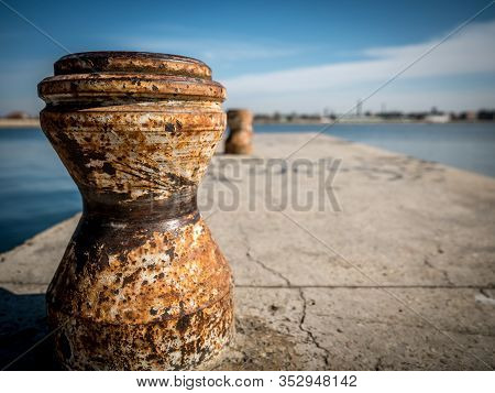 Rusty Ship Mooring Bollard On A Dock With Water And Blue Sky In The Background. Mooring Bollard On L