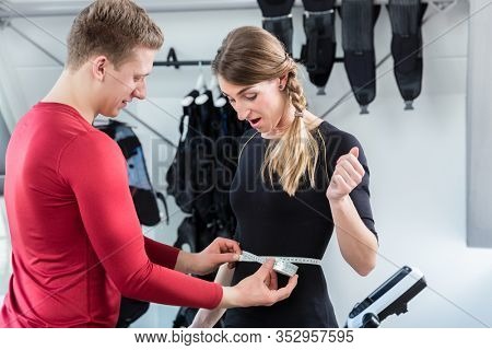 Coach measuring stomach circumference of woman in ems gym with tape