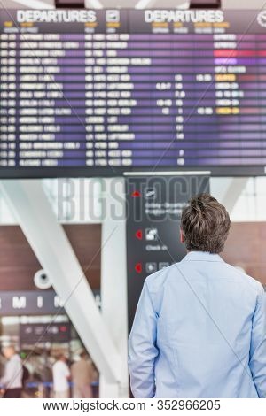 Rear view of mature man looking at his flght on screen in airport