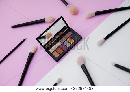 Side View Of Colorful Metallized Eyeshadow Pallete And Natural Makeup Brushes On White And Pink Back
