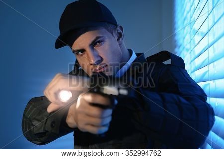 Professional Security Guard With Flashlight And Gun Near Window In Dark Room