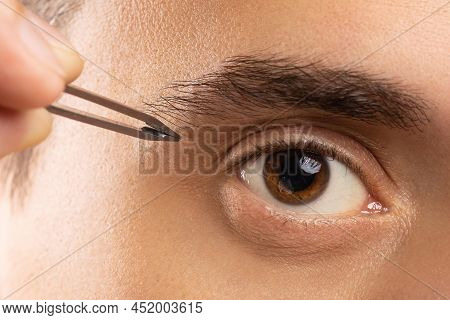 Male Eye And Tweezers For Eyebrow Shape Correction