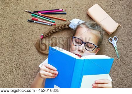 A Girl On The Floor Reads A Book When She Is Tired Of Sitting At A Desk Or Table