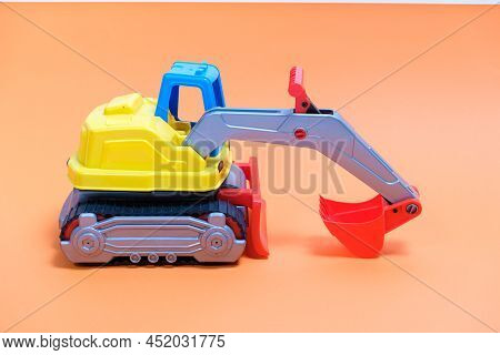 Yellow Excavator Plastic Car On Orange Background. Construction Machinery Car For Digging For Toy St