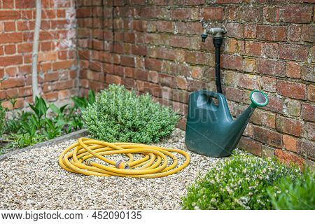 Watering Can, Garden Hose (hosepipe) And Outside Tap In A Uk Back Garden. Gardening Scene