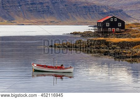 Small boat and black wooden house, Djupivogur, Eastfjords, Iceland. Landscape shot in autumn with mountain background.
