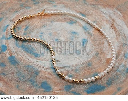 White Pearl Golden Necklace On Beige Blue Spotted Textured Background