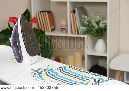 Iron On The Ironing Board And Childrens Striped T-shirt. Care Of Clothing, Ceramic Soleplate.
