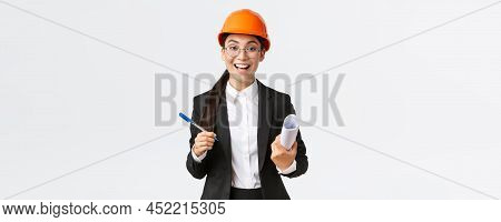 Smiling Professional Female Architect, Asian Engineer In Helmet And Business Suit, Holding Blueprint