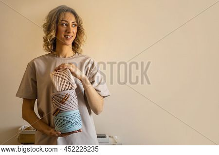 Happy Young Creative Blonde Female Holding Pile Of Hank Reel Ribbon Yarn Standing At Home