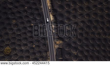Above Landscape View Of Black Sand Gound For Volcanic Vineyard And Long Straight Road With White Car