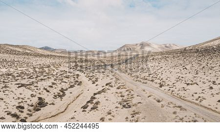 Path Road In The Middle Of A Mountains Sand Desert With Blue Bright Sky In Background. Concept Of De