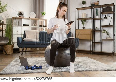 Happy Fitness Woman Training On Swiss Ball In Living Room. Portrait Of Muscular Woman Enjoying Home 