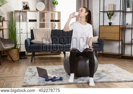 Young Caucasian Woman In Black Sports Leggings And A White T-shirt With Smart Phone Sitting On Fit B