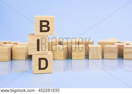 On A Bright Blue Background, Light Wooden Blocks And Cubes With The Text Bid