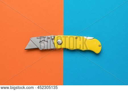 Stylish Folding Yellow Knife On A Blue And Orange Background. Minimalistic Concept. Flat Lay.