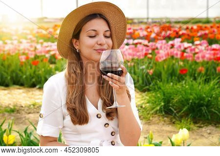 Beautiful Woman Smells Precious Red Wine With Closed Eyes In Garden With Blossomed Flowers On Backgr