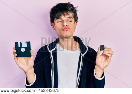 Handsome hipster young man holding floppy disk and sdxc card looking at the camera blowing a kiss being lovely and sexy. love expression. 