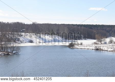 Sunny April Day On The Shore Of The Lake. Bare Branches Of Bushes And Birches. Blue Sky.