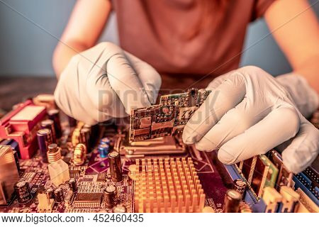 The Engineer's Gloved Hand Holds The Chip Board On The Background Of The Motherboard. The Concept Of