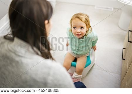 Cute Child Girl Sitting On Chamberpot On The Bathroom Look At Is Mother