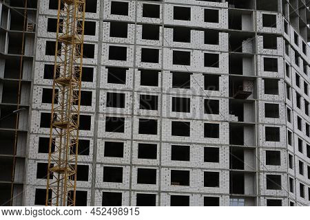 Construction Yellow Crane Builds A Tall Multi-apartment Residential Building From White Bricks And C